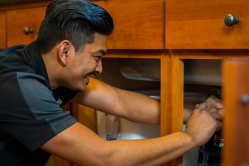 Licensed plumber using professional leak detection equipment inside a home.