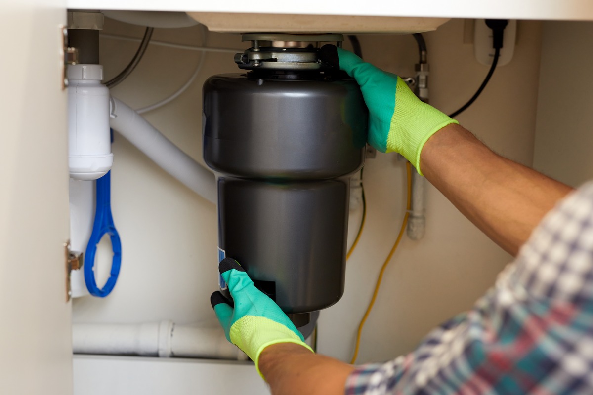 Licensed plumber installing a garbage disposal beneath a kitchen sink