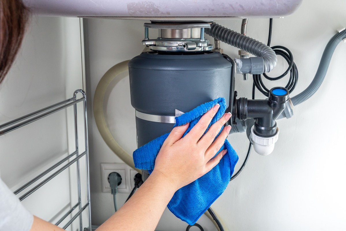 Licensed plumber repairing a garbage disposal beneath a kitchen sink